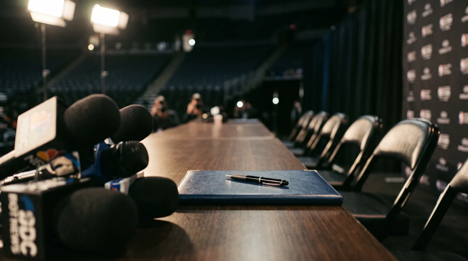 Microphones and a closed contract folder with a pen on an empty press conference table