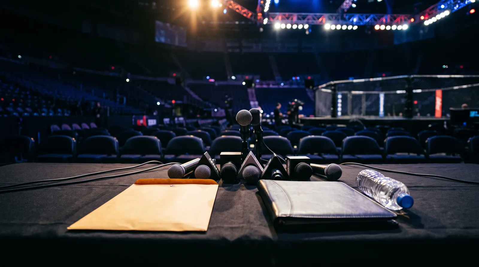 Microphones on an empty press conference table beside an envelope and a contract folder