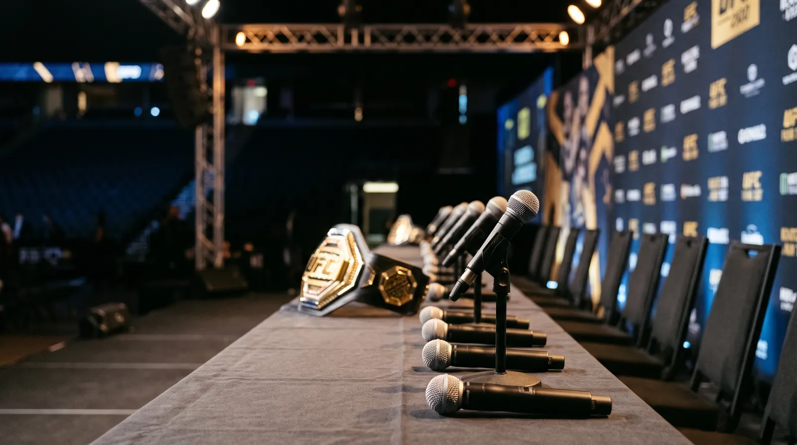 Microphones and a championship belt on a press conference table under spotlights