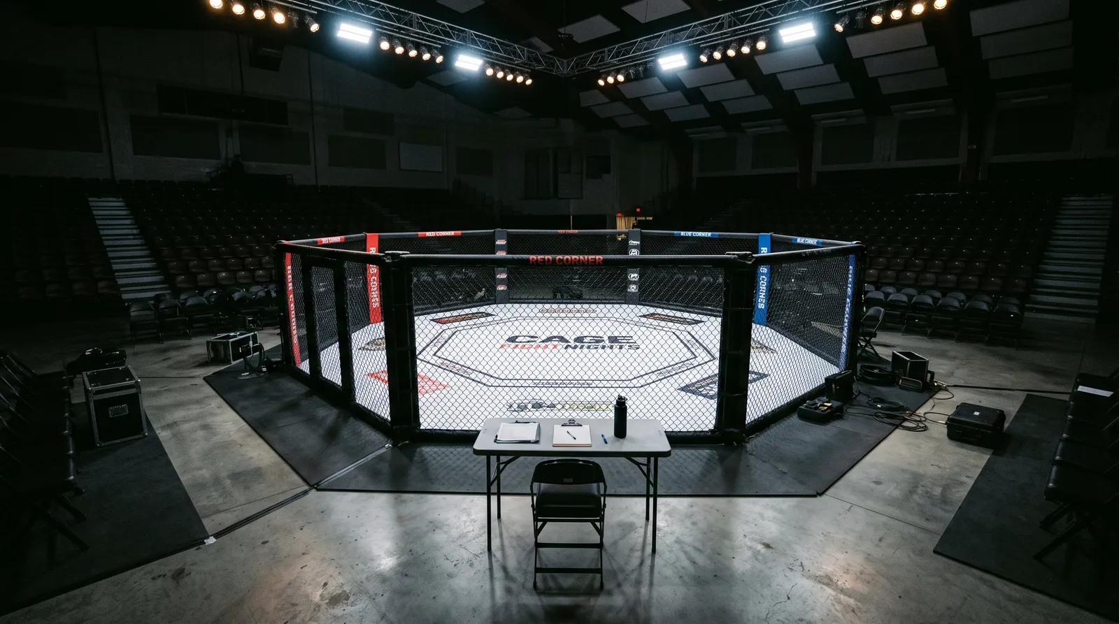 An empty octagon under work lights with a lone cageside chair before a Contender Series card