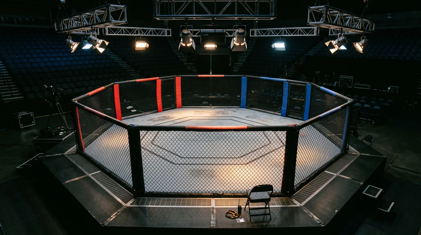 An empty octagon under work lights with a staff lanyard and radio resting cageside
