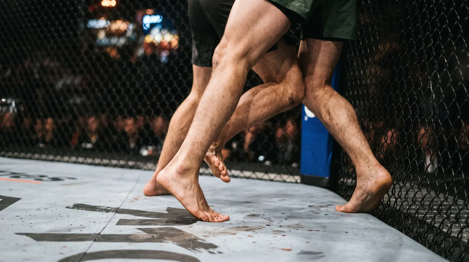 Two fighters' feet and legs scrambling on the canvas against the octagon fence as one tries to stand up