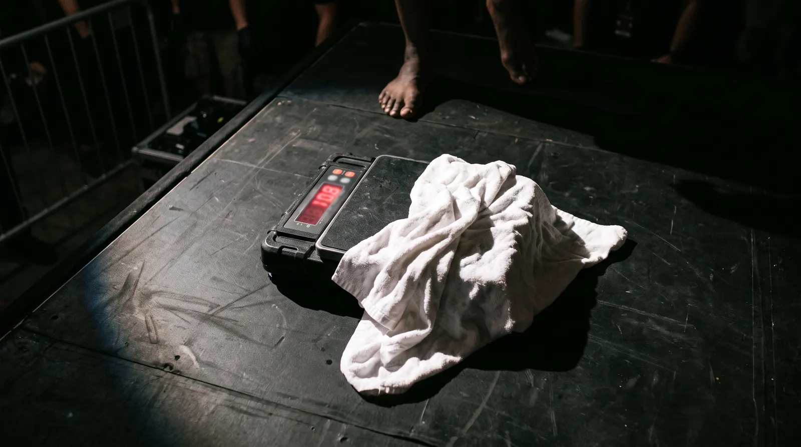 A weigh-in scale on a dark stage with a towel draped over it under a single spotlight