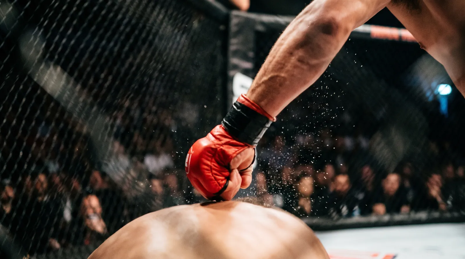 A gloved fist landing an overhand punch with sweat flying off the glove under arena lights