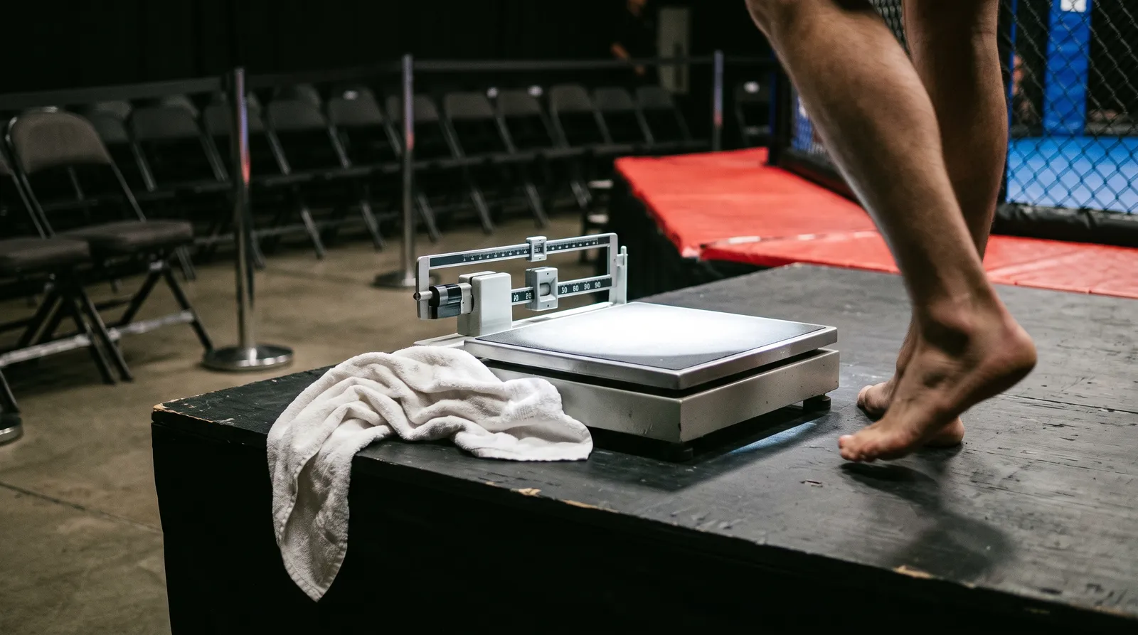 A weigh-in scale with a towel draped over it under harsh stage lighting