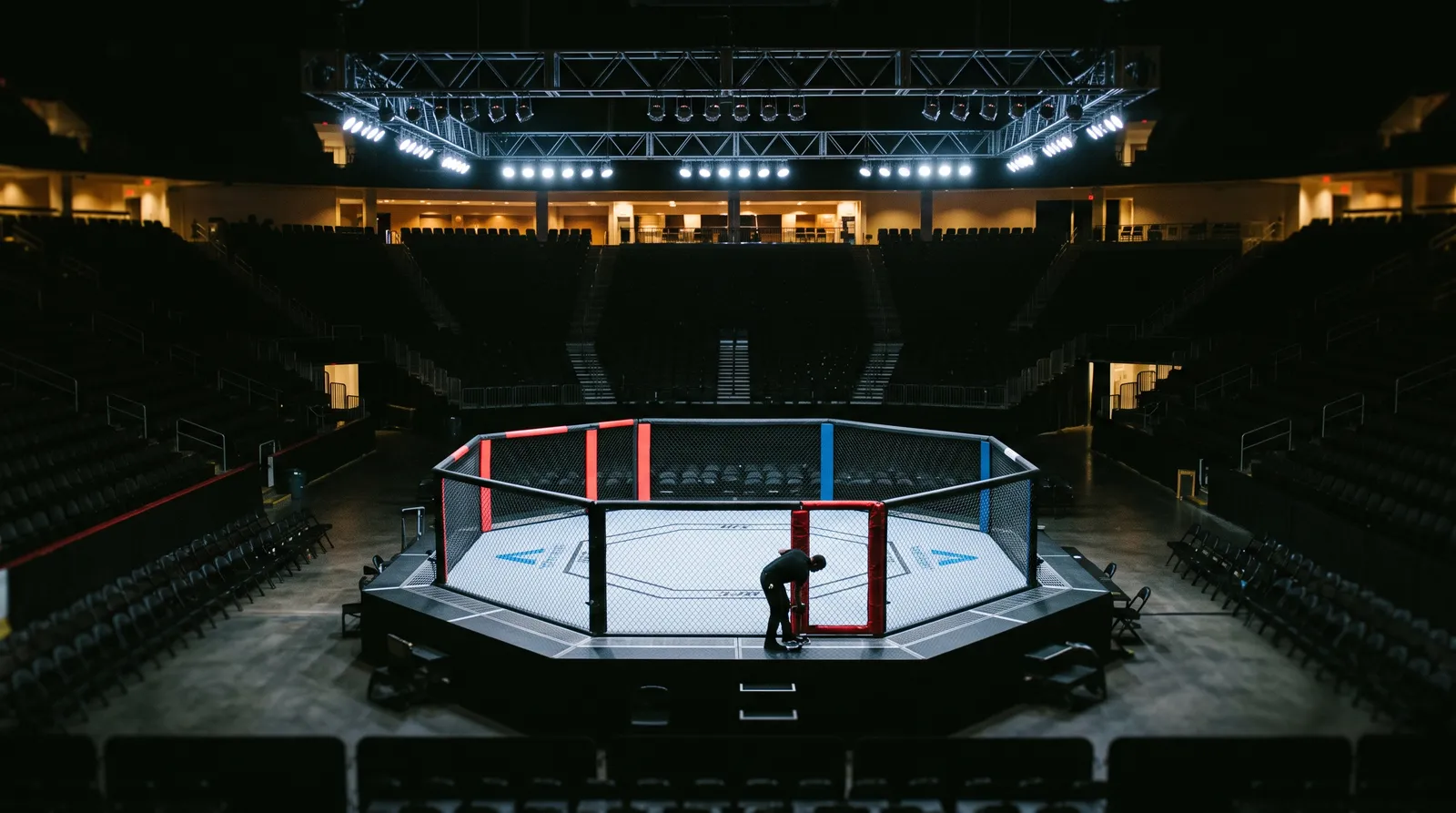 An empty octagon under work lights in a darkened arena before fight week