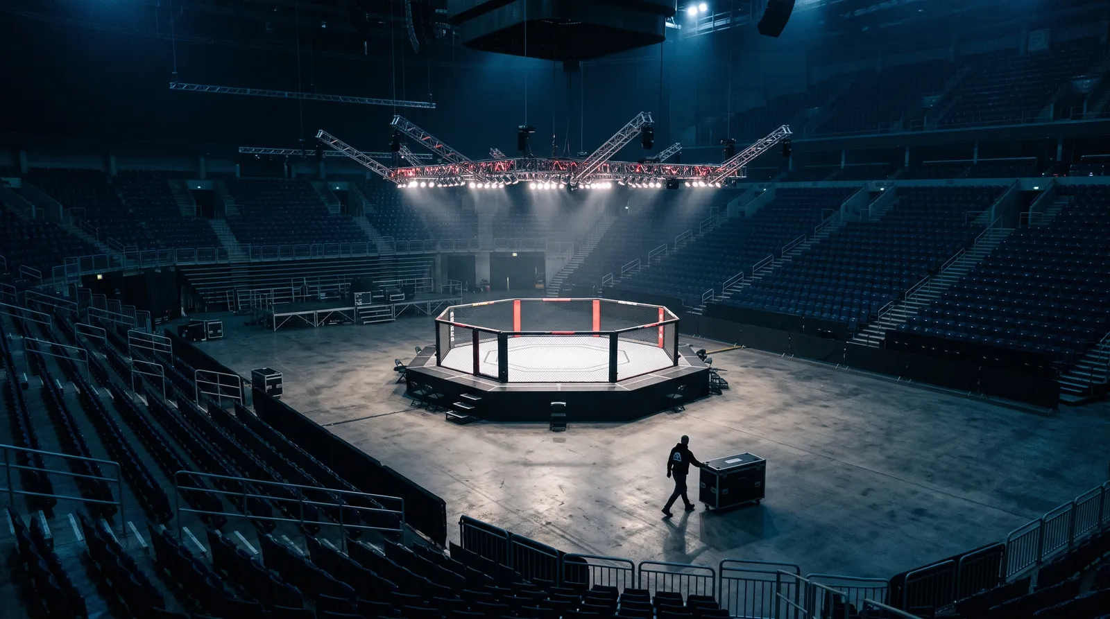 An empty octagon lit by work lights in a dark arena before a UFC event