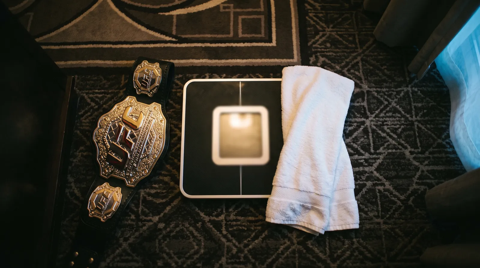 A championship belt and a towel next to a weigh-in scale under warm light