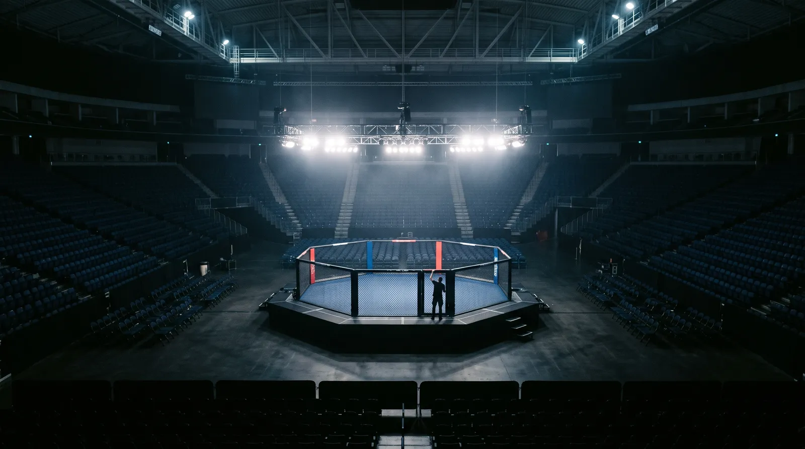 An empty octagon under work lights in a darkened arena before a UFC event