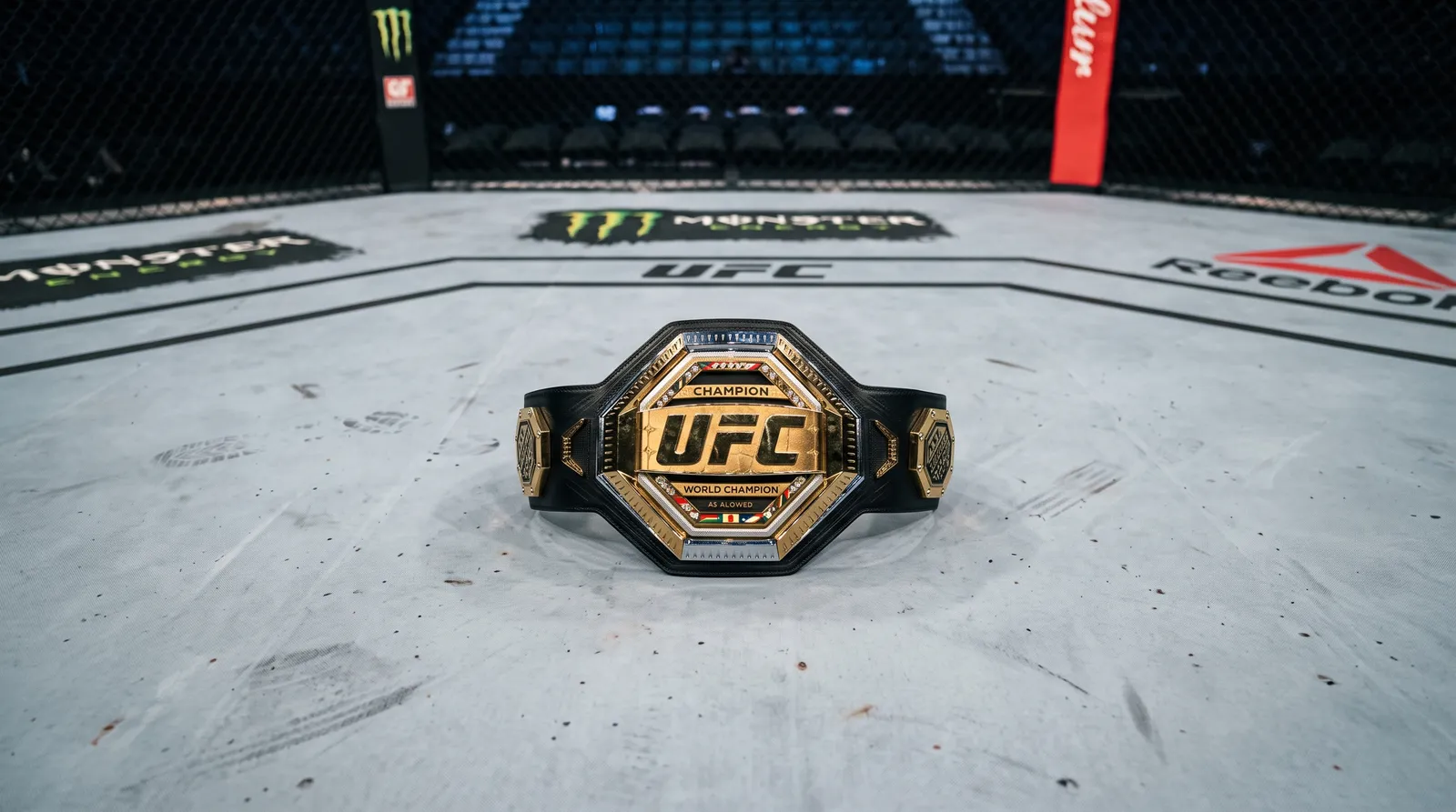 A championship belt resting on an empty octagon canvas under work lights