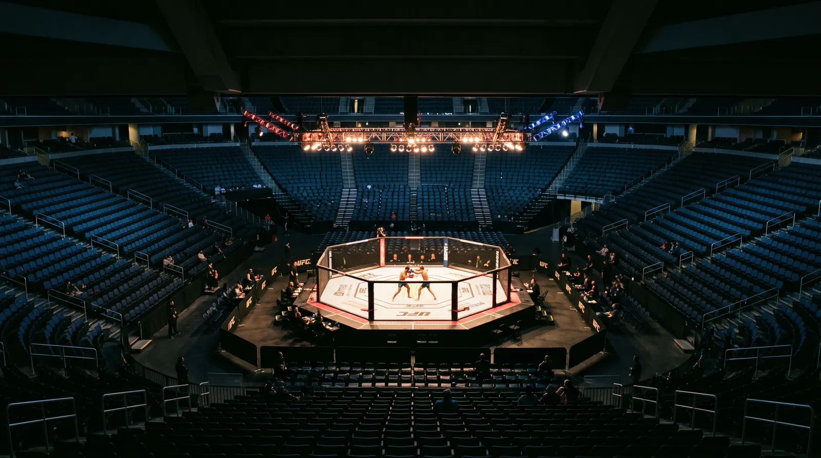 Two fighters trade strikes in a brightly lit octagon surrounded by a mostly empty arena during early prelims