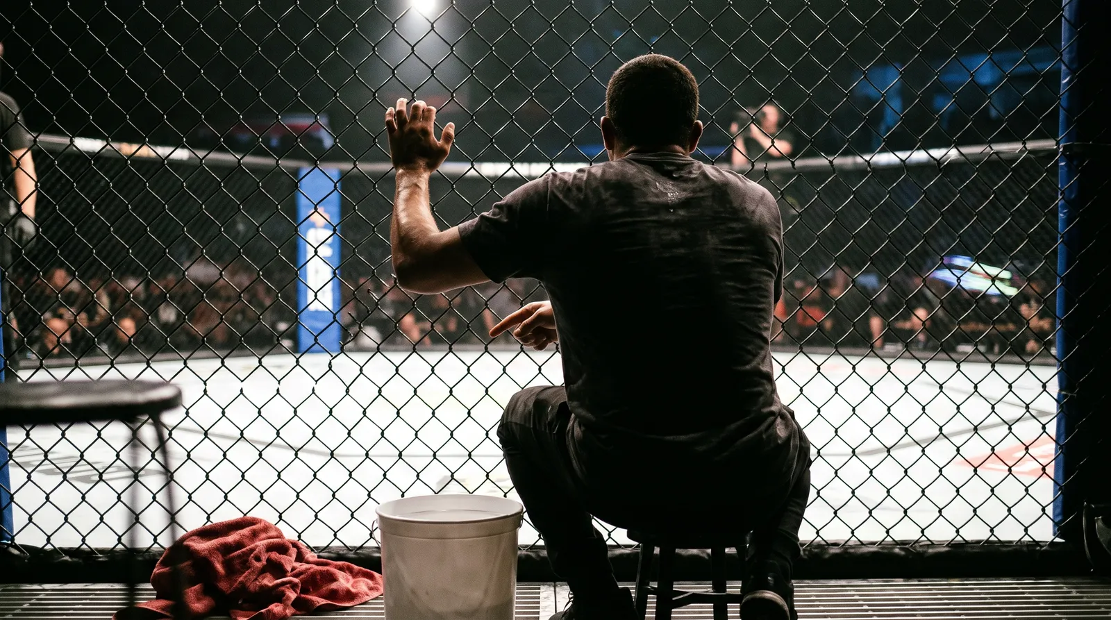 A coach shouting instructions from the corner of an octagon beside a stool and bucket
